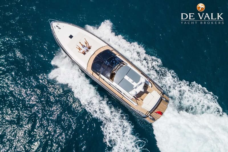 Een witte motorboot met houten dek vaart over blauw water, met twee personen zonnend op de boeg. — Baia Italia 70