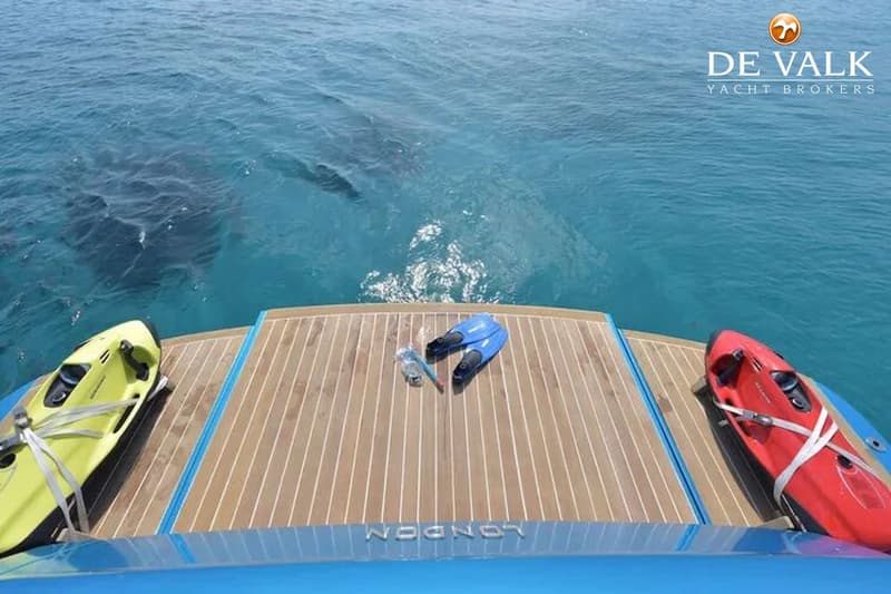 Een boot met een teakhouten dek, twee waterscooters, zwemvliezen en een snorkelset, met de naam "LONDON" op de spiegel.