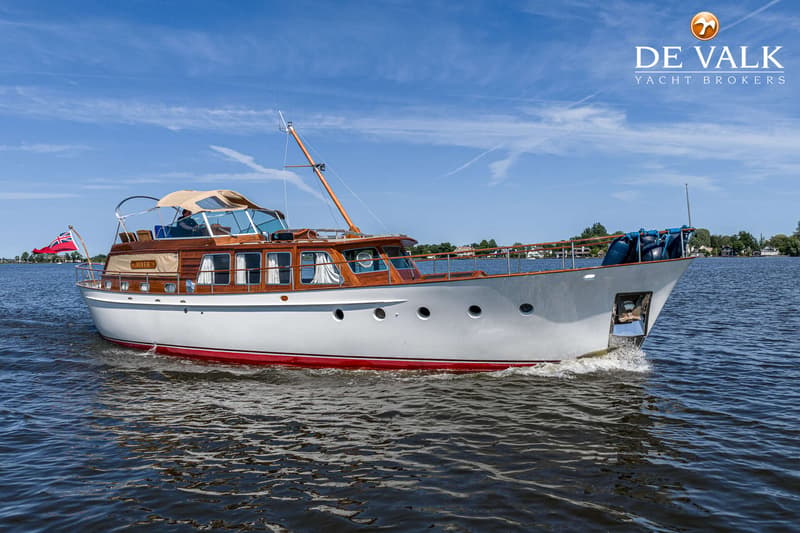 Een witte motorboot met houten opbouw en een rode streep op de romp vaart over water onder een blauwe lucht.