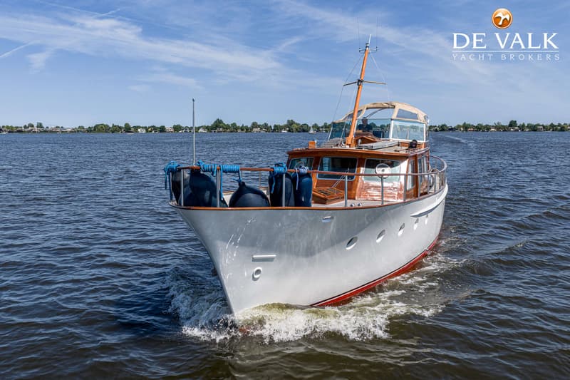 Een witte motorboot met een houten opbouw vaart op een meer onder een blauwe lucht. — Kok Spitsgatkotter 16.50