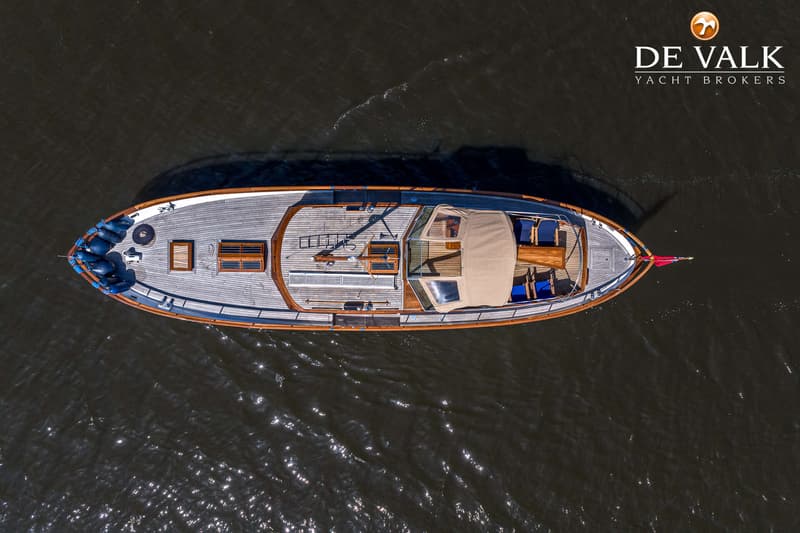 Een bovenaanzicht van een boot met een houten dek en een beige cabriokap, drijvend op donker water.