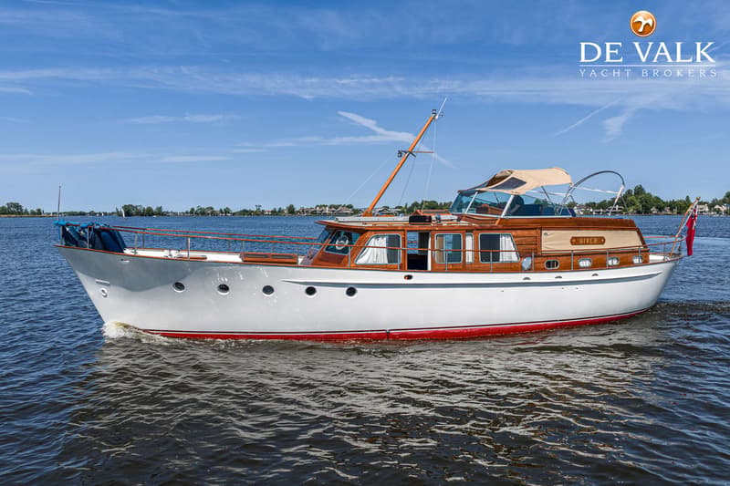 Een witte motorboot met houten opbouw en rode waterlijn vaart op een meer onder een blauwe lucht. — Kok Spitsgatkotter 16.50