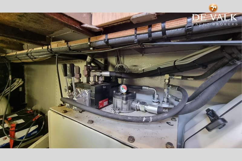 Een detailfoto van een hydraulisch systeem met slangen, meters en hendels, naast twee accu's.
