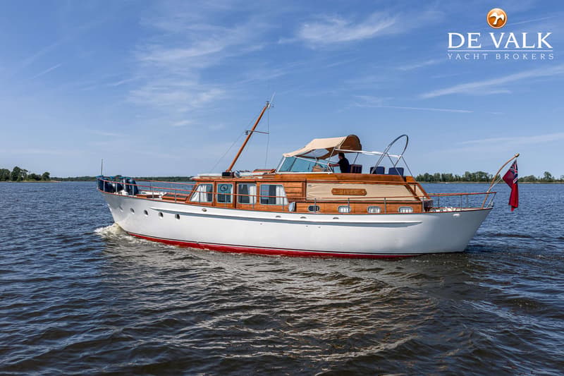 Een witte motorboot met houten opbouw en rode waterlijn vaart op een meer onder een blauwe hemel. — Kok Spitsgatkotter 16.50