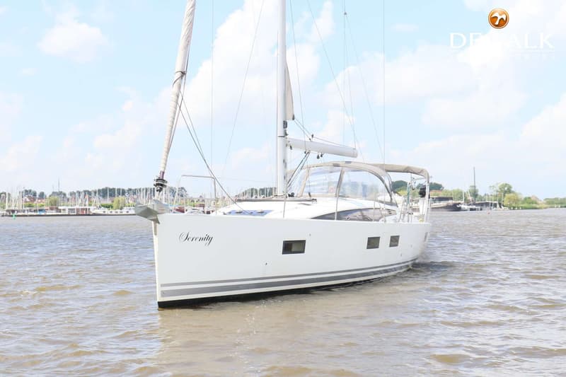 Een witte zeilboot met de naam "Serenity" vaart op een waterweg, met een jachthaven op de achtergrond. — Jeanneau 54