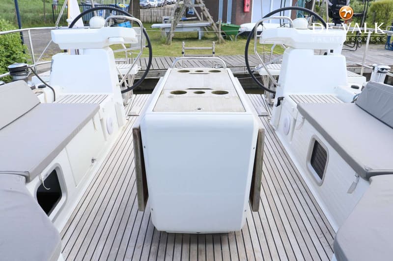 De foto toont het achterdek van een boot met twee stuurwielen, een houten tafel en grijze kussens op de banken. — Jeanneau 54