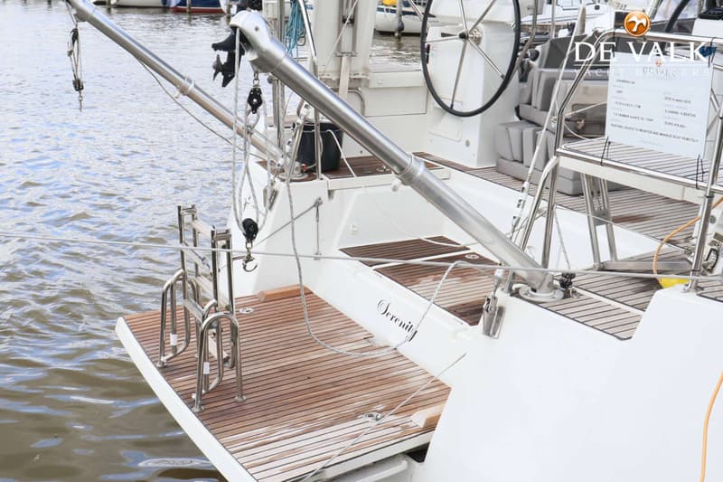 De achtersteven van een witte zeilboot met een teakhouten dek, een zwemplateau en de naam "Serenity" erop. — Jeanneau 54
