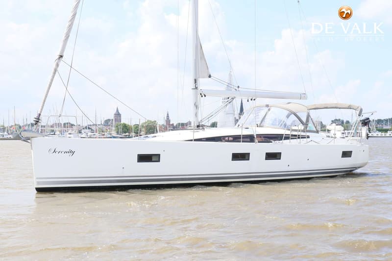 Een witte zeilboot met de naam "Serenity" vaart op water, met een stadje op de achtergrond. — Jeanneau 54