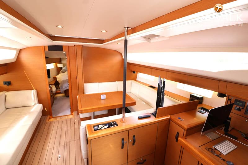 De foto toont het interieur van een boot met een houten vloer, houten wanden en witte banken rond een houten tafel.