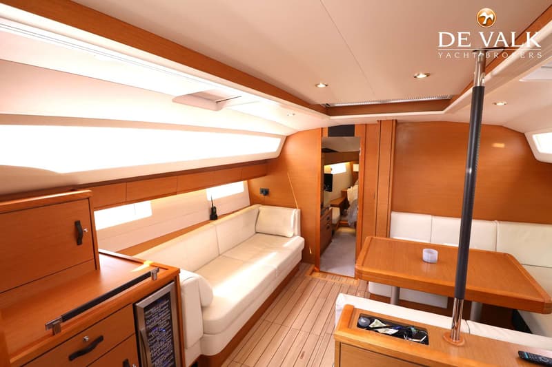 De foto toont het interieur van een boot met houten wanden en vloer, witte banken, een tafel en een wijnkoeler. — Jeanneau 54