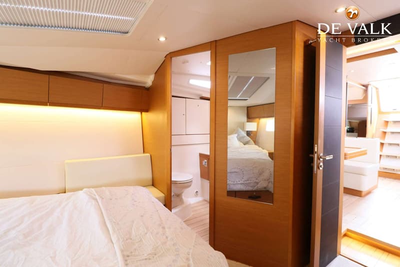 De foto toont een slaapkamer in een boot met een wit bed, houten wanden en een spiegeldeur die een toiletruimte weerspiegelt.