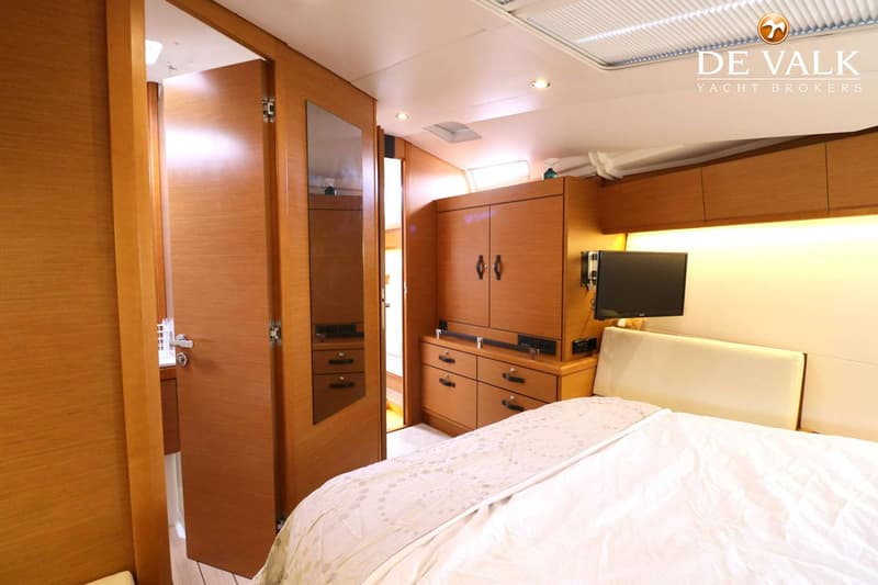 Een slaapkamer in een boot met een tweepersoonsbed, houten kasten, een televisie en een spiegel. — Jeanneau 54