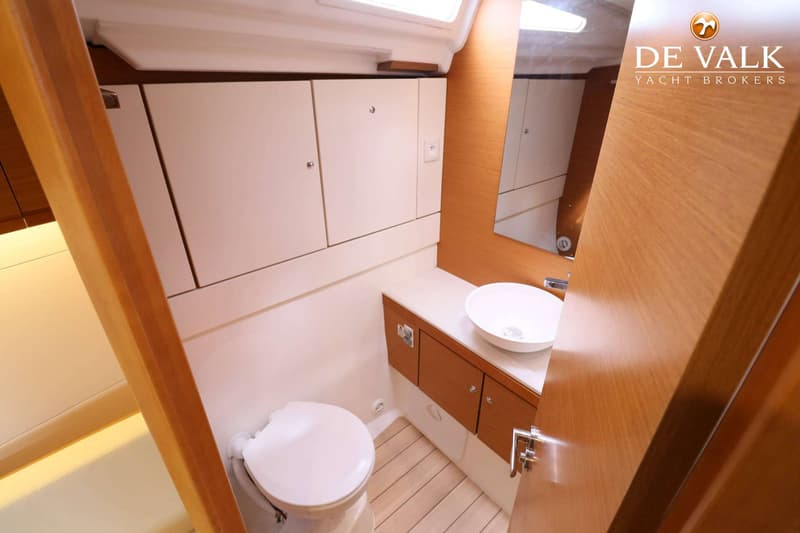 Een badkamer in een boot met een toilet, wastafel, spiegel en houten en witte kasten. — Jeanneau 54