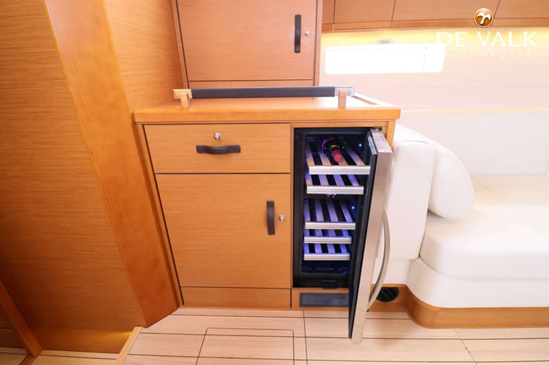 Een houten interieur met een ingebouwde wijnkoeler, laden en kasten, naast een witte bank.