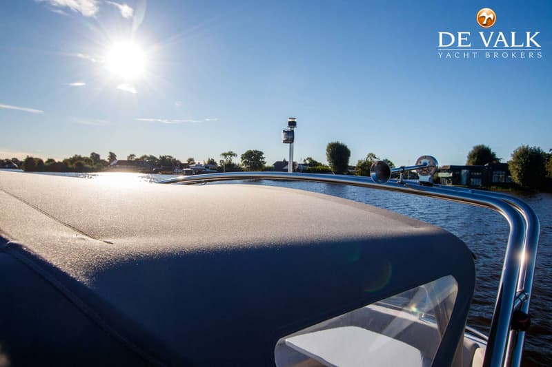Een boot met een donkerblauwe kap en een glimmende reling, varend op water met de zon laag aan de horizon.