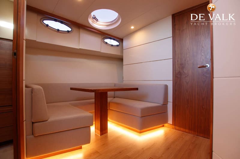 Een kajuit met een U-vormige bank, een houten tafel, patrijspoorten, een dakluik en een houten deur.