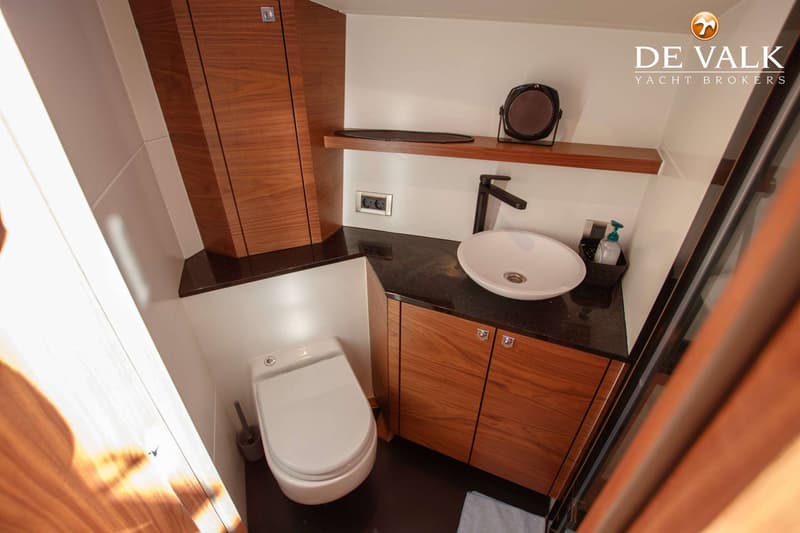 Een badkamer met een wit toilet, een witte wasbak op een donker aanrechtblad, en houten kasten en planken.
