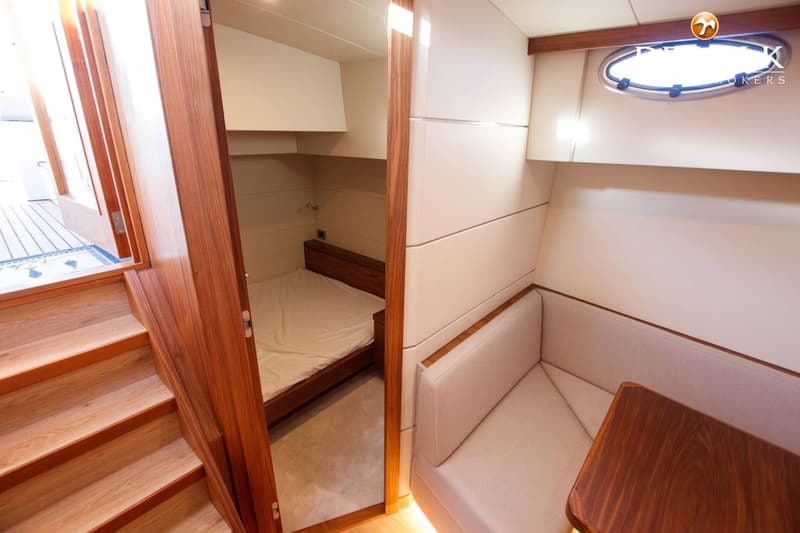 De foto toont een interieur van een boot met een trap, een slaapkamer en een zithoek met een tafel.