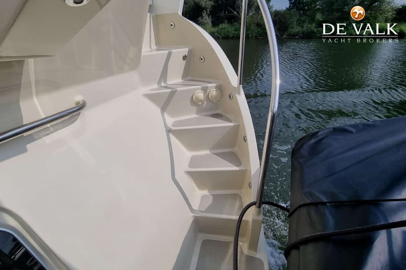 Een witte boot met een trap naar het dek, een reling en een zwart afdekzeil op het water. — Vischer Yachting Custom 125AC