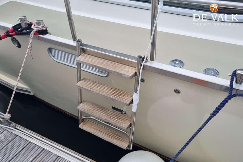 Een boot met een zwemtrap, afgemeerd aan een steiger met touwen en stootwillen. — Vischer Yachting Custom 125AC