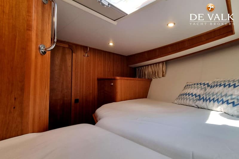 Een kajuit met twee bedden, houten wanden, een dakluik en een logo van "DE VALK YACHT BROKERS".
