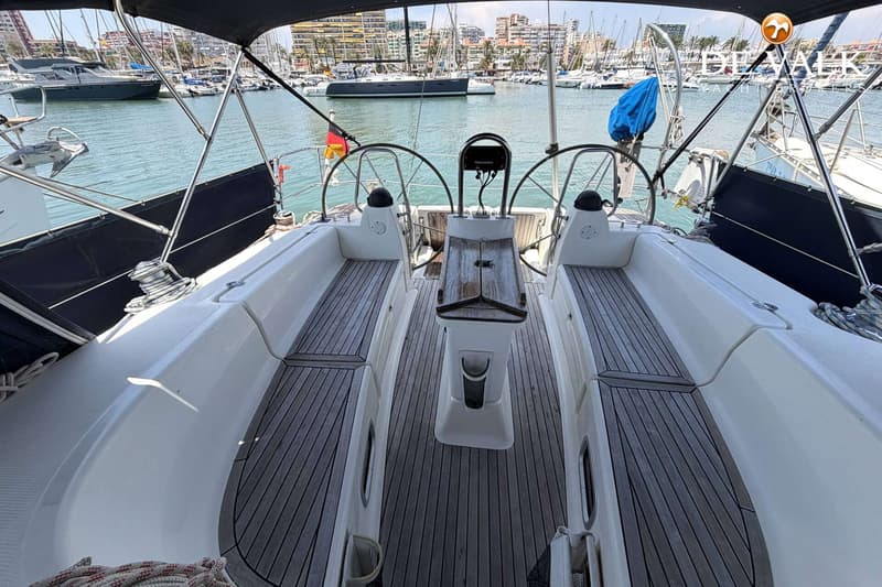 Een bovenaanzicht van de kuip van een zeilboot met twee stuurwielen en een houten tafel, liggend in een haven.