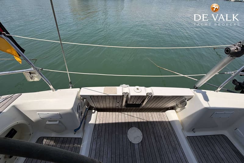 De foto toont het achterdek van een boot met een houten vloer en een wit luik, met water op de achtergrond.