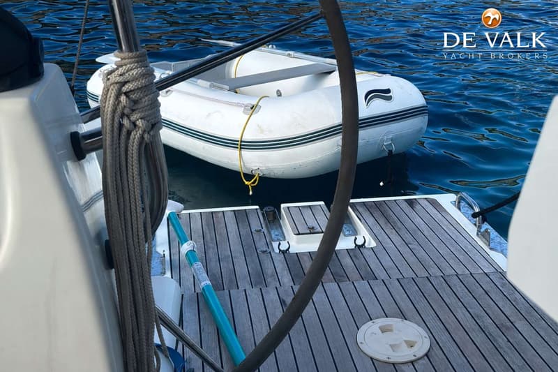 Een witte rubberboot met een zwarte streep en een groen-witte streep drijft achter een boot met een houten dek.