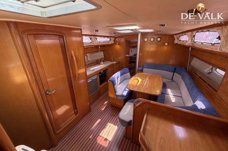 De foto toont het interieur van een boot met een houten afwerking, een kombuis, een zithoek en een kajuit.