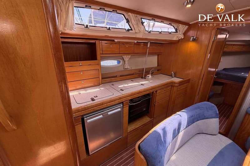 Een houten interieur van een boot met een kombuis, ramen, een koelkast, een fornuis en een blauwe bank. — Bavaria 40 Cruiser
