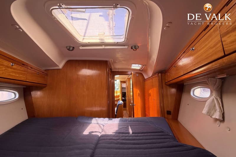 De foto toont een kajuit met een bed, houten kasten en een patrijspoort met een gordijn. — Bavaria 40 Cruiser