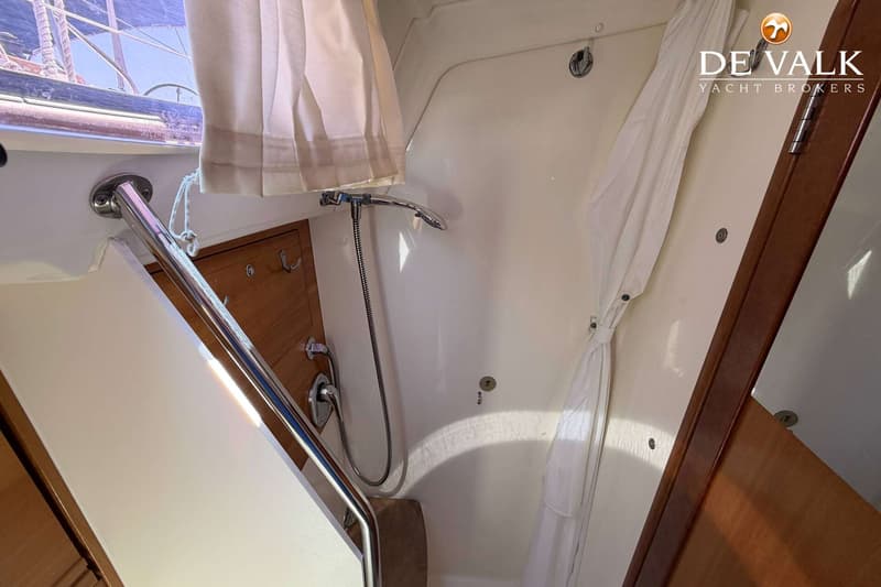 De foto toont een badkamer of doucheruimte op een boot, met een douchekop, witte gordijnen en houten accenten.