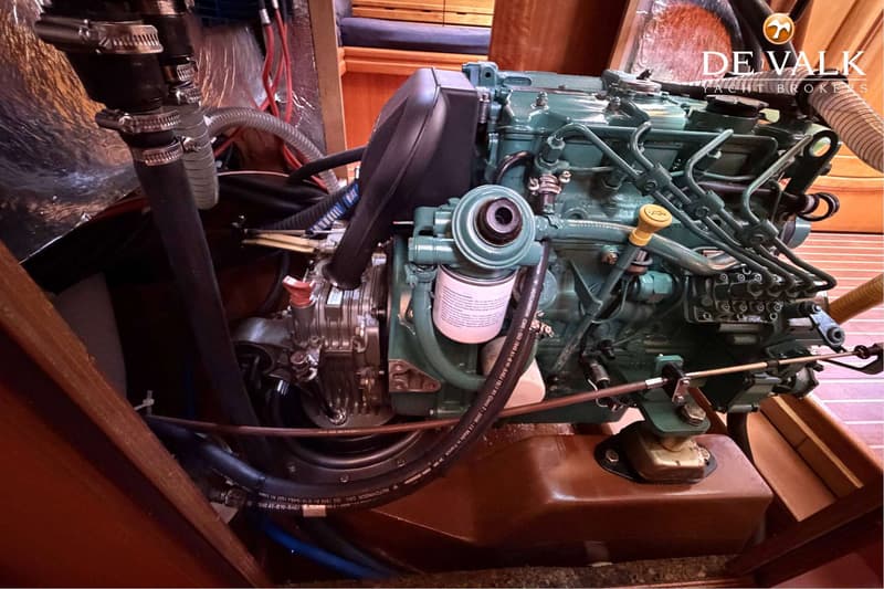Een groene scheepsmotor met diverse slangen, kabels en een oliefilter, gemonteerd in een houten interieur.
