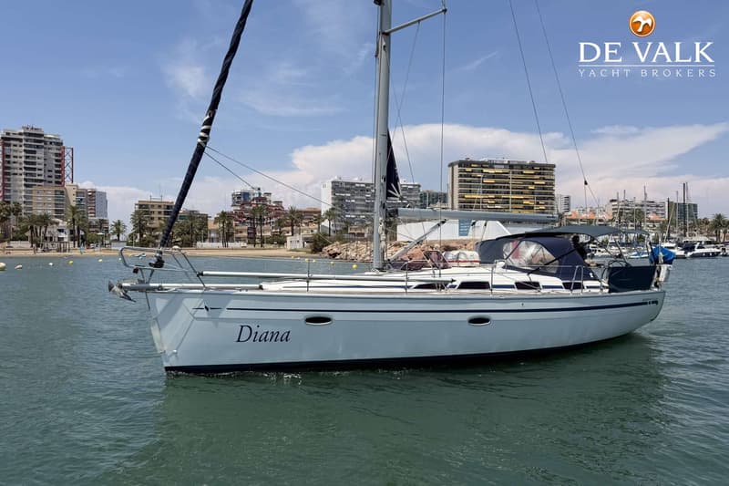 Een witte zeilboot met de naam "Diana" ligt in het water, met een stad aan de kust op de achtergrond. — Bavaria 40 Cruiser