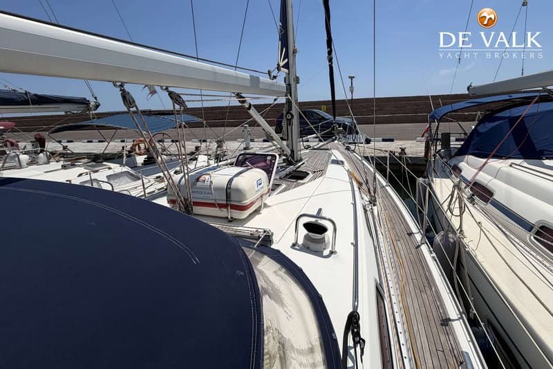 Een bovenaanzicht van het dek van een zeilboot met een reddingsvlot en een blauwe buiskap, liggend naast een andere boot.
