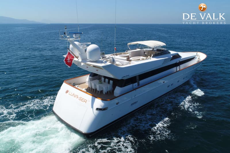 Een witte motorjacht met de naam "LUNA-SEA" vaart op open water, met een rode vlag met wit kruis aan de achterkant.
