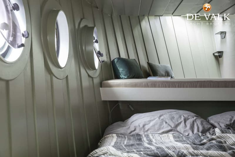 De foto toont een kajuit met twee bedden, drie patrijspoorten en een leeslampje. — Qrooz Floating Appartment