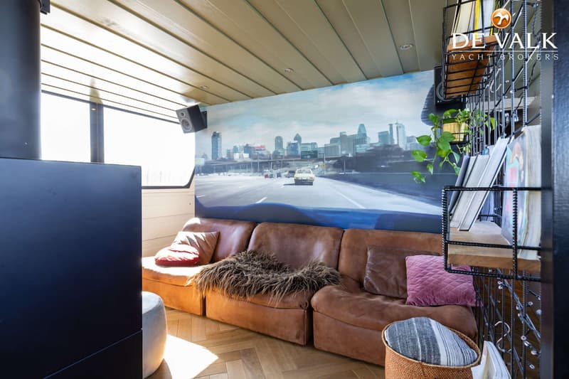 Een interieur met een bruine leren bank, een muurschildering van een snelweg en een zwart metalen rek met boeken.