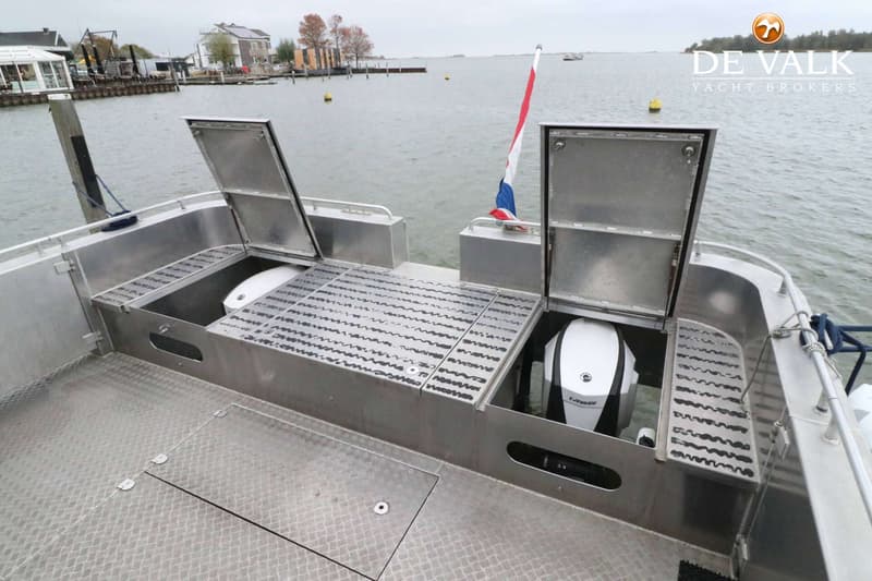 De achterkant van een aluminium boot met twee open luiken waar buitenboordmotoren onder zitten, een Nederlandse vlag en een…