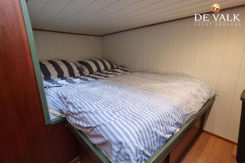 Een kajuit met een tweepersoonsbed met gestreepte lakens en kussens, omringd door houten panelen.