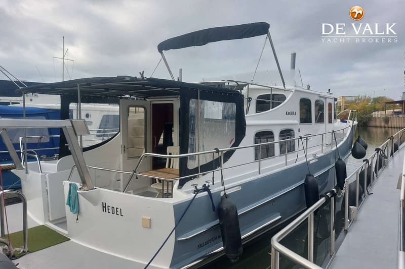 Een witte en grijze motorboot met de naam "KOBRA" en "HEDEL" ligt aangemeerd onder een bewolkte hemel.