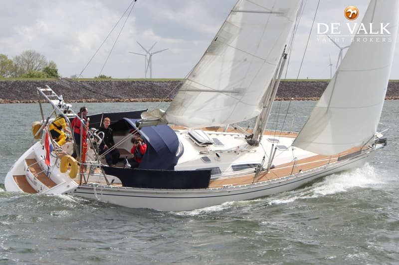 Een witte zeilboot met teakhouten dek en blauwe buiskap vaart op ruw water met vier personen aan boord. — Comfortina 42