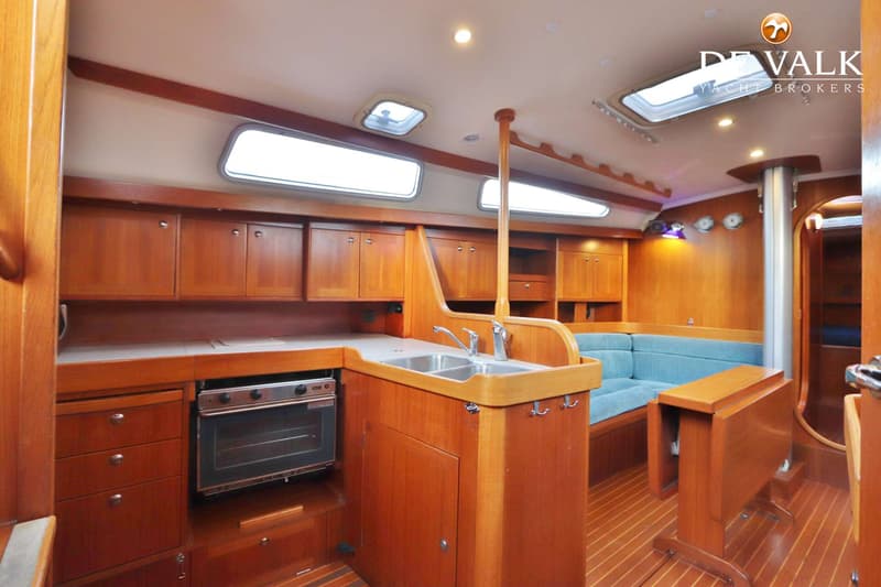 De foto toont het interieur van een boot met een houten afwerking, een kombuis met oven en dubbele spoelbak, en een zithoek…