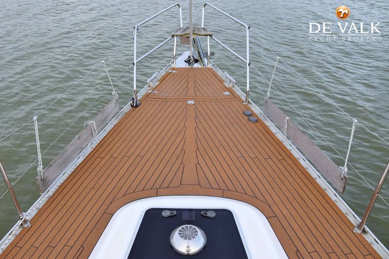De foto toont het voordek van een boot met een bruin dek en een witte opbouw, omringd door water. — Comfortina 42