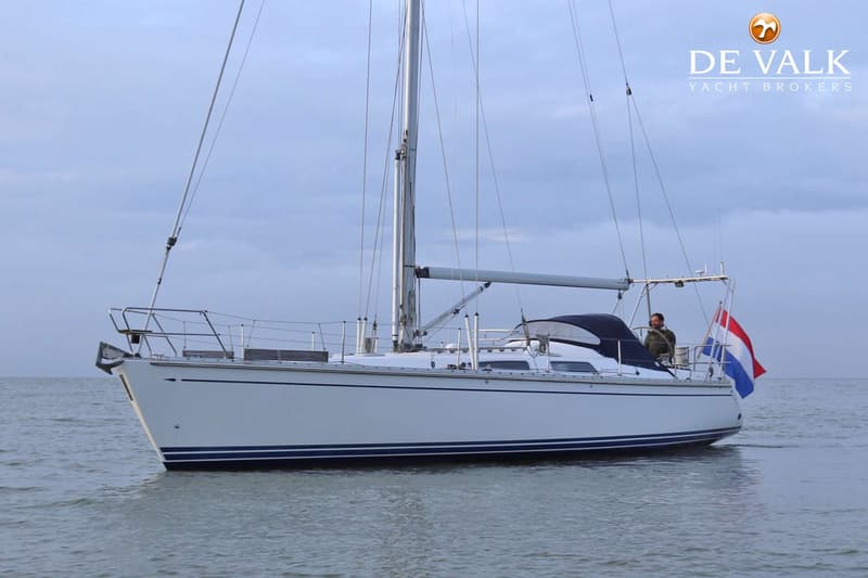 Een witte zeilboot met blauwe strepen op de romp vaart op kalm water onder een bewolkte lucht. — Comfortina 42