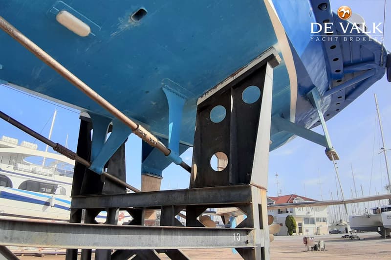 De onderkant van een blauwe boot staat op een metalen bok, met een roer en schroefas zichtbaar.