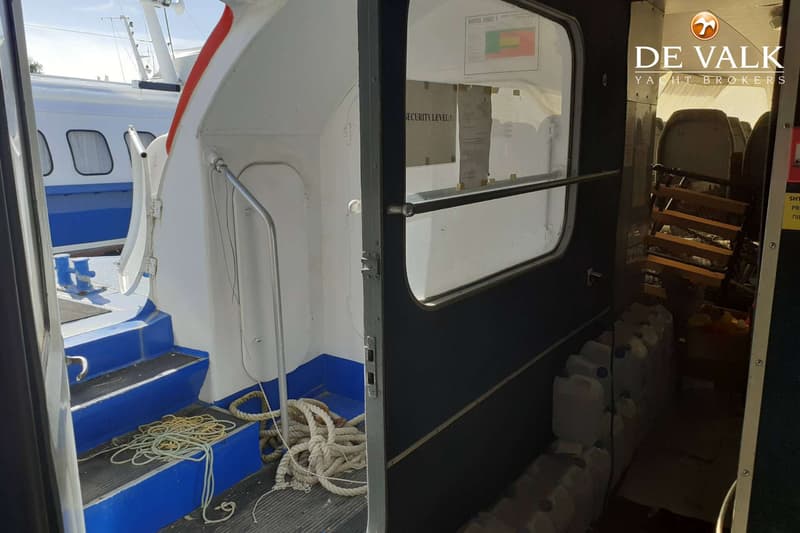 Een open deur van een boot met een trap naar beneden, touwen op de vloer en jerrycans in de kajuit.