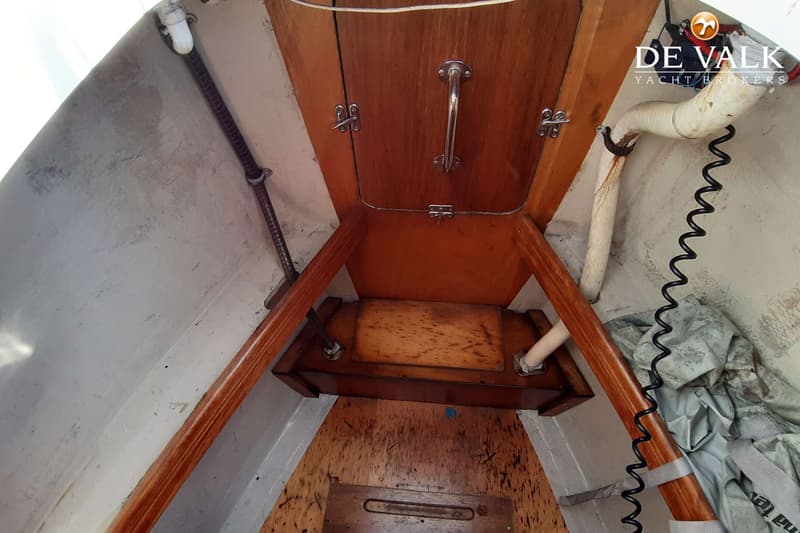De foto toont een interieur van een boot met houten panelen, een handvat, en een grijze vloer met een houten luik.