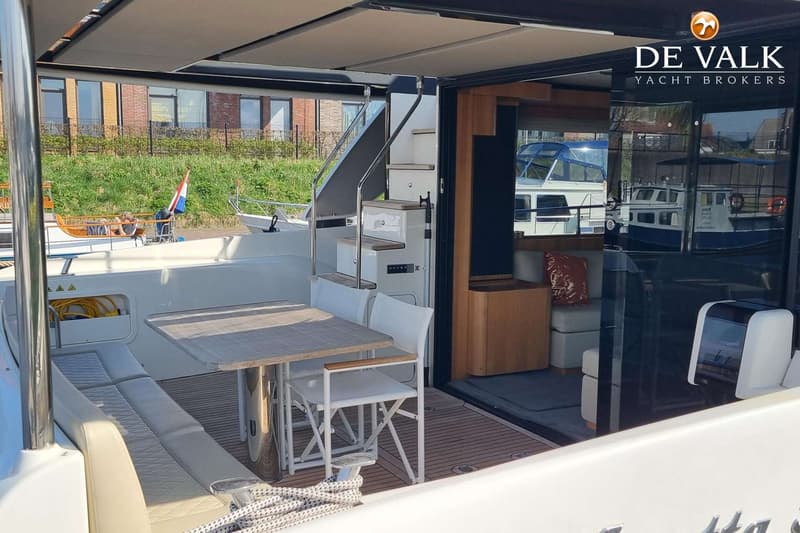 Een achterdek van een boot met een tafel, stoelen, een bank, een trap naar een hoger dek en een open toegang tot de kajuit.