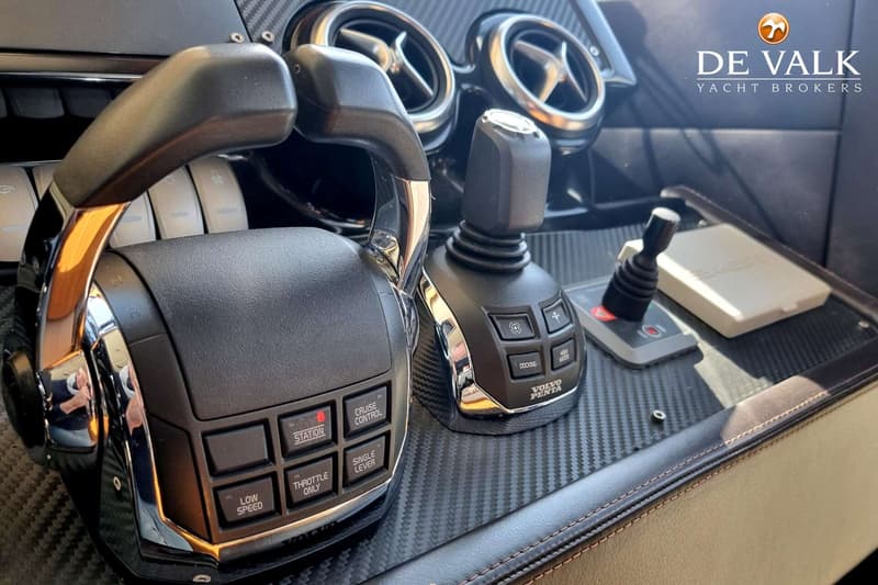 Een detailfoto van een bootstuurstand met een Volvo Penta joystick en gashendels, en een De Valk Yacht Brokers logo.